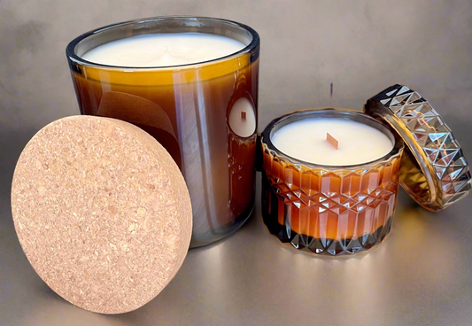 Two candles in decorative glass holders on a reflective surface with a textured background.